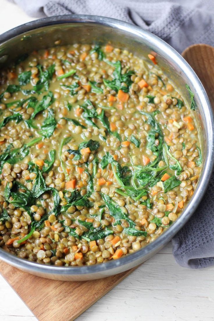 a pot filled with lentils and spinach on top of a wooden cutting board