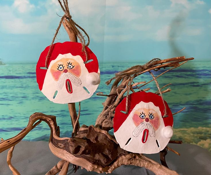 two santa claus ornaments hanging from a tree branch in front of a painting on the wall