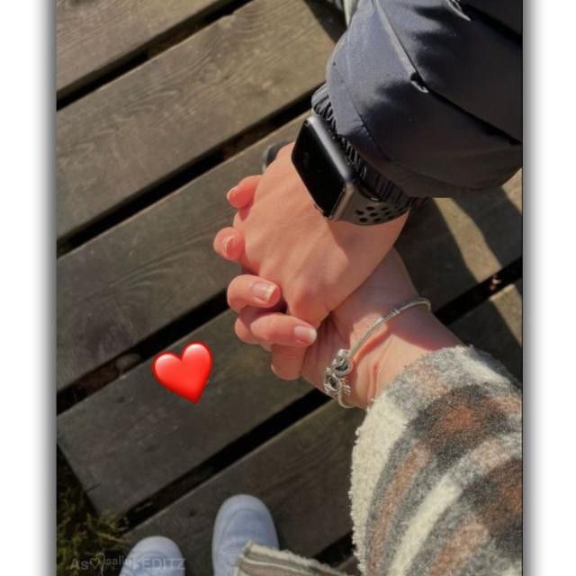 two people holding hands while standing next to each other on a wooden deck with a red heart in the middle