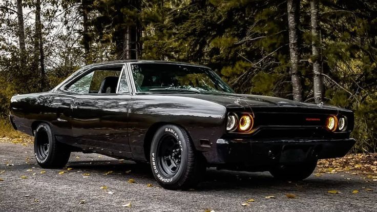 an old muscle car parked on the side of a road in front of some trees