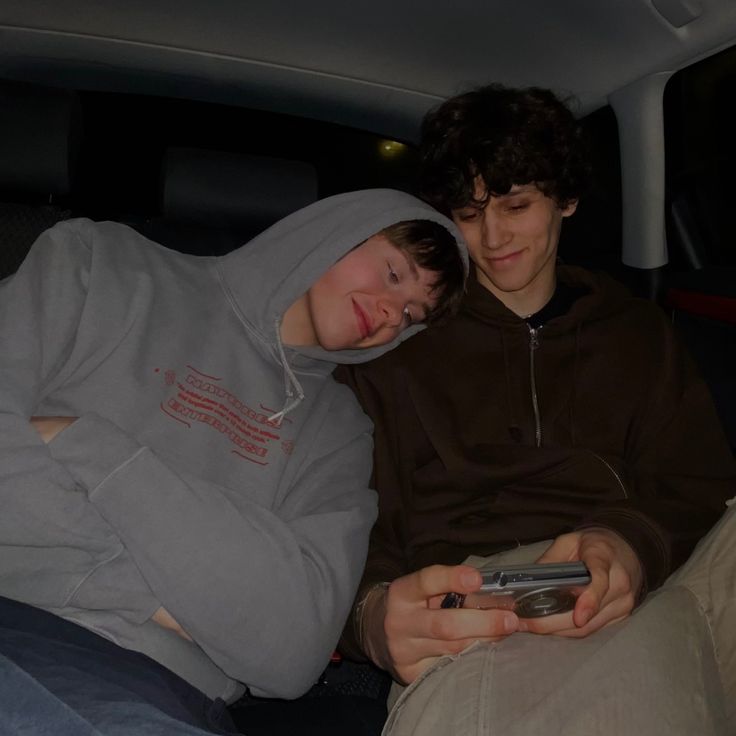 two people sitting in the back of a car, one holding a cell phone and smiling