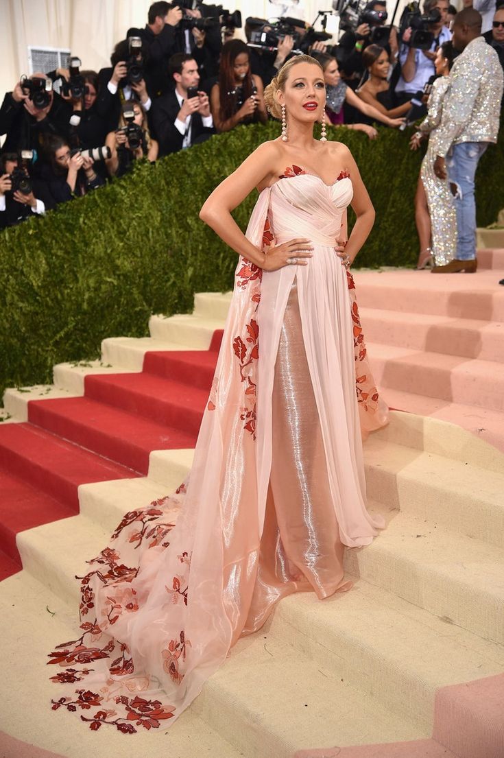 a woman in a pink gown standing on steps with cameras around her and people taking pictures