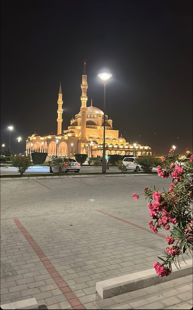 a large building lit up at night with flowers in the foreground