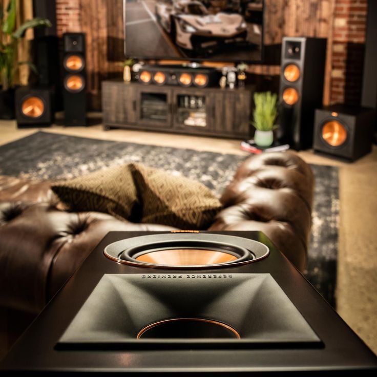 a speaker sitting on top of a brown couch in front of a tv and speakers