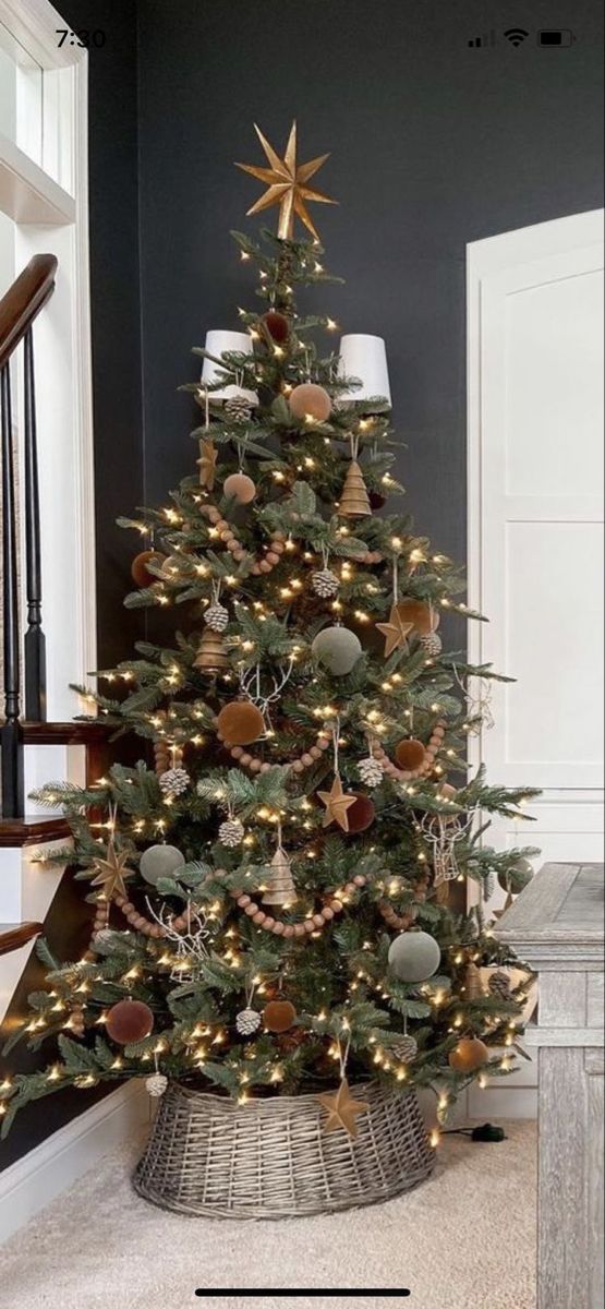 a christmas tree with lights and ornaments in a basket on the floor next to stairs