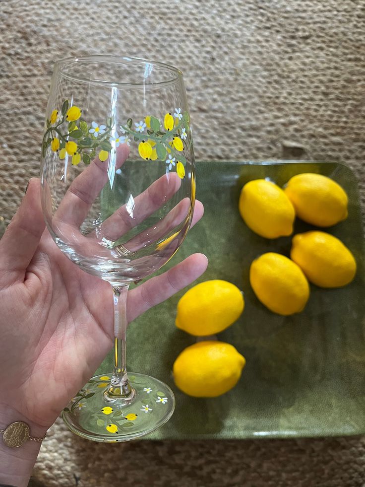 a person holding a wine glass in front of some lemons on a green tray