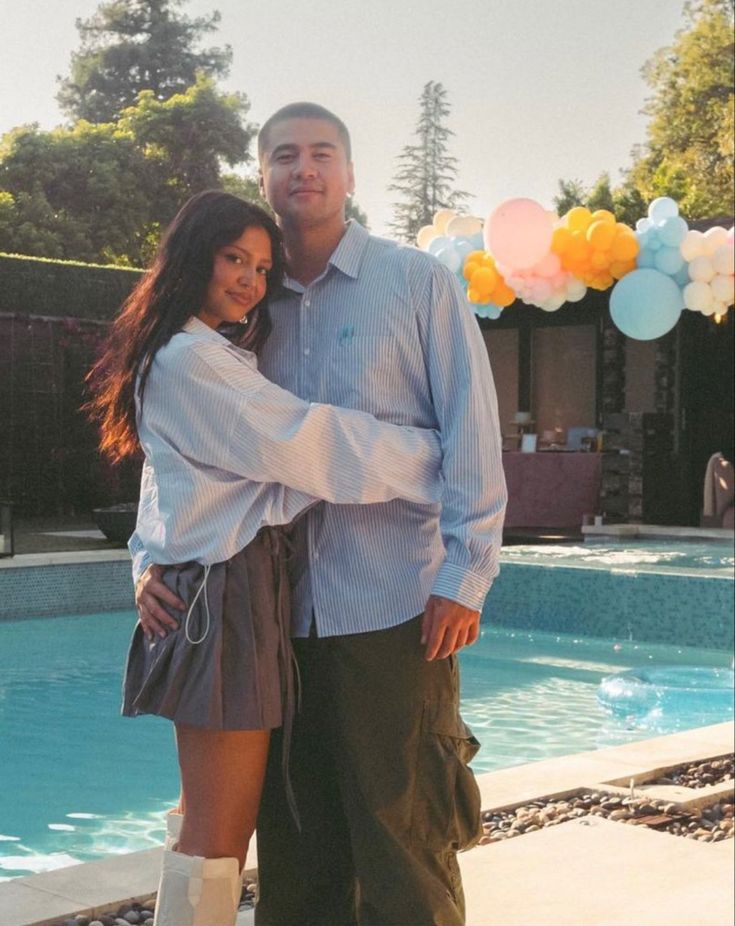 a man and woman standing next to each other near a pool with balloons in the background