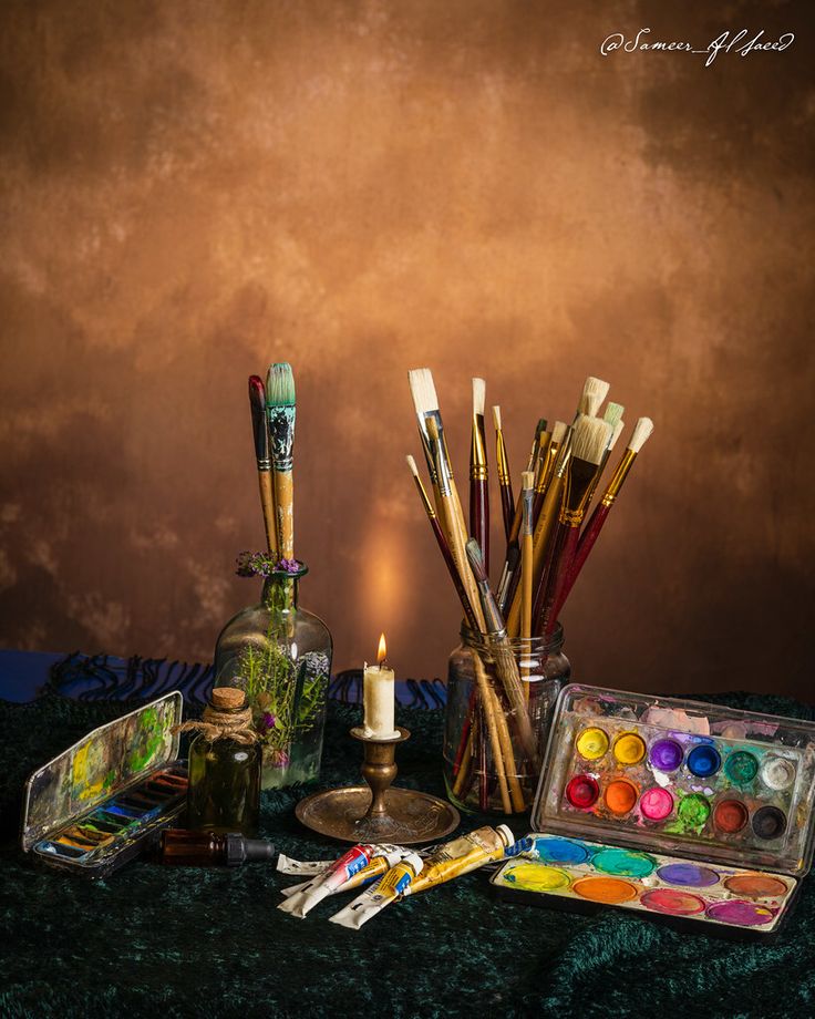 an assortment of art supplies including paint, brushes and candles on a green table cloth