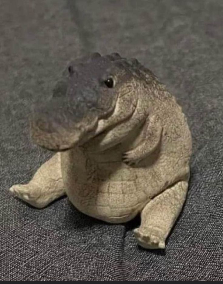 a small toy alligator sitting on top of a gray floor next to a black and white wall