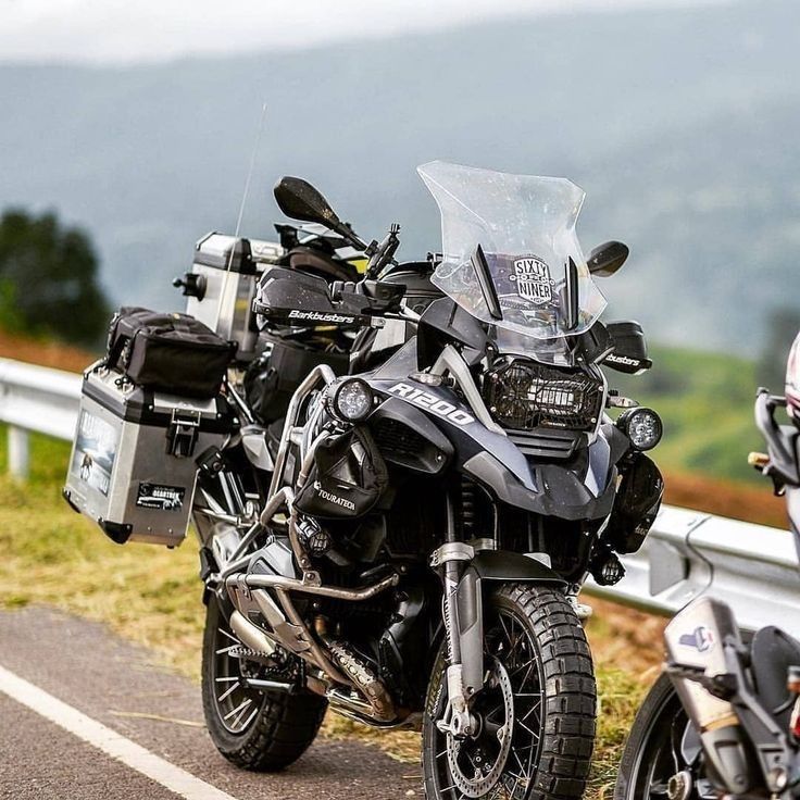 two motorcycles parked next to each other on the side of a road with mountains in the background