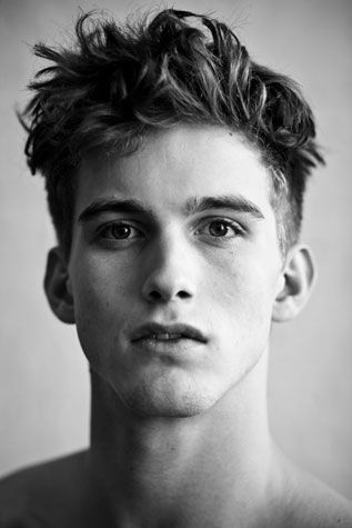 black and white photograph of a young man with messy hair looking at the camera while wearing no shirt