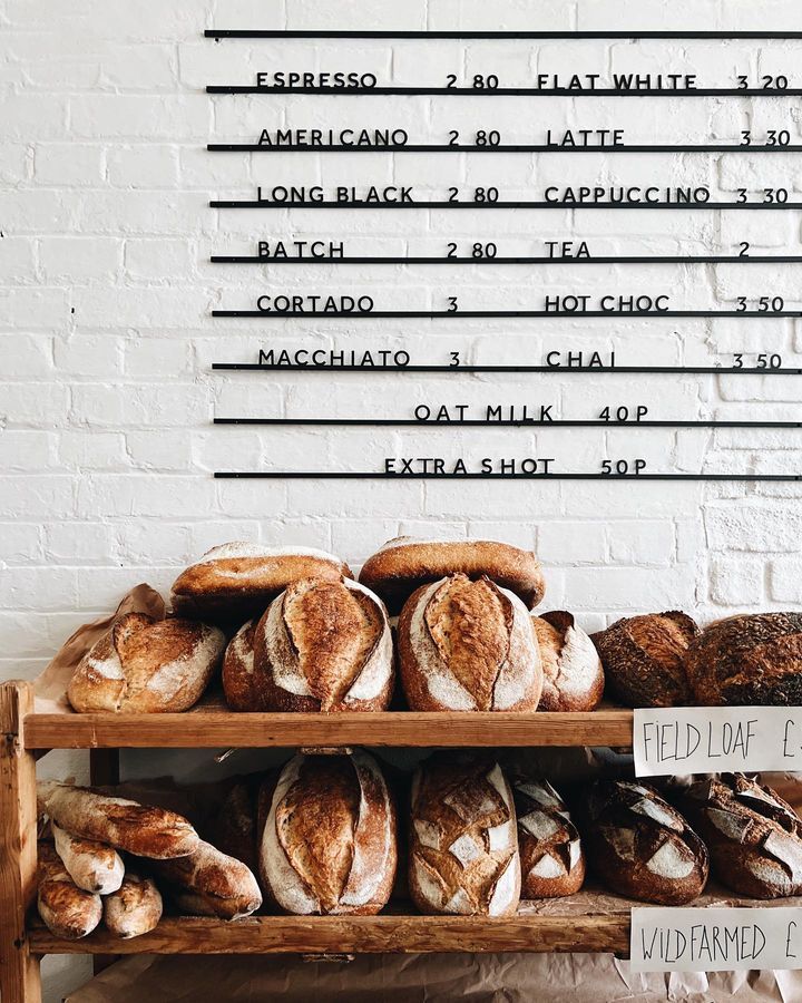 breads and pastries are on display in front of a white brick wall with black writing