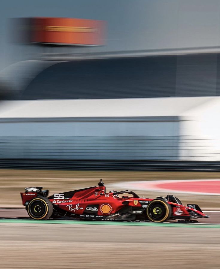 a red race car driving on a track with blurry buildings in the back ground