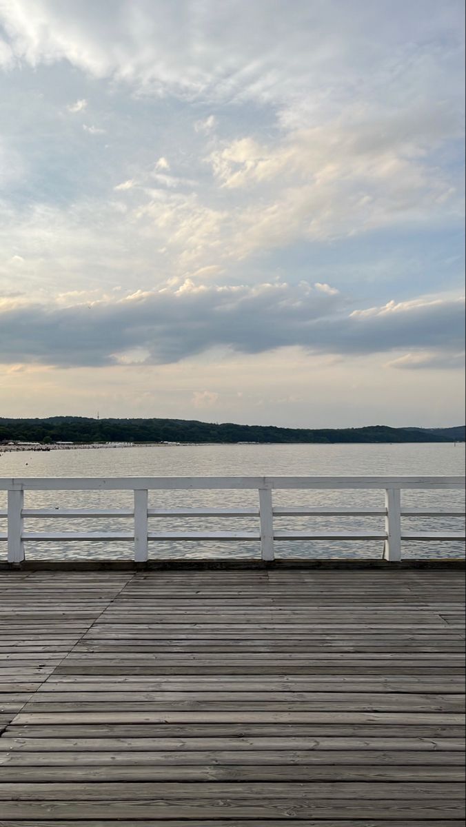 a bench sitting on top of a wooden pier next to the ocean under a cloudy sky