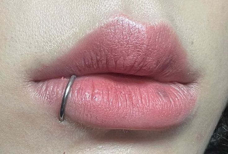 a woman's lips with pink lipstick on her cheek and ring around the lip