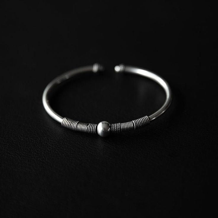 This finely crafted, stackable beauty is delicately adorned with a central bead and intricate twisted wire detailing. Crafted to be seamlessly stacked with other bracelets, this piece is a versatile addition to your collection.   Design: by NOIR KĀLA Material: 925 Silver Size: 7 cm x 6 cm Weight: 14 g Adjustable Simple Bangle Jewelry, Sterling Silver Wire Wrapped Bangle, Sterling Silver Wire Wrapped Bangle Jewelry, Adjustable Metal Bracelet With Oxidized Finish, Adjustable Oxidized Finish Bracelets, Adjustable Spiral Jewelry With Oxidized Finish, Minimalist Silver Beads Round Jewelry, Dainty Metal Beaded Bracelets, Minimalist Round Silver Beads Jewelry