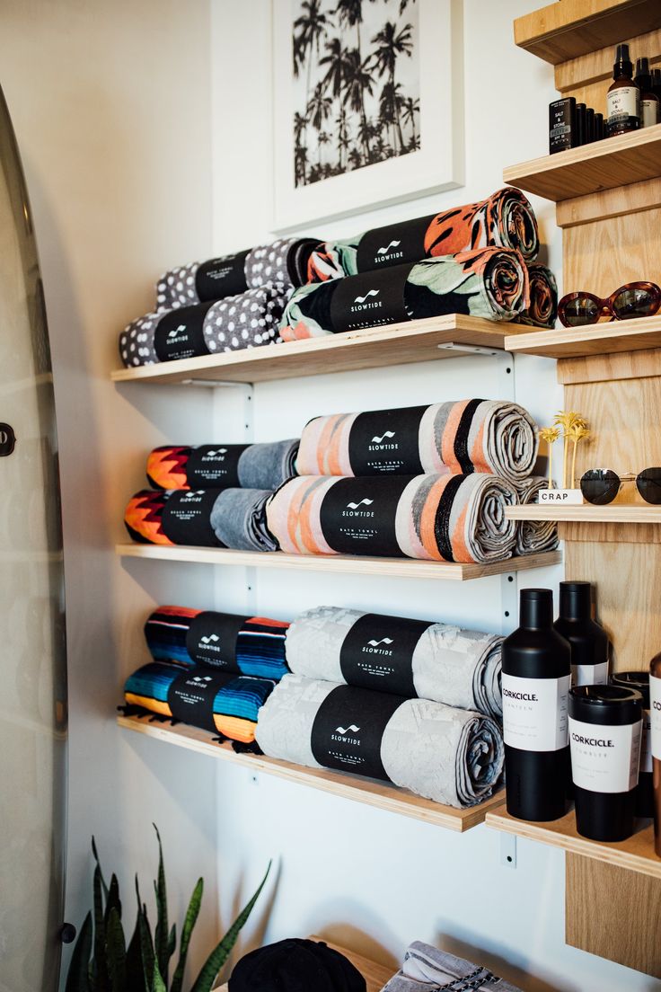 towels and other items are on shelves in a room with wooden shelvings, including a surfboard