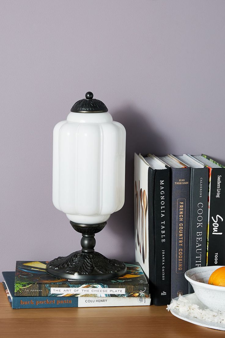 a table topped with books and a white lamp next to a bowl of oranges