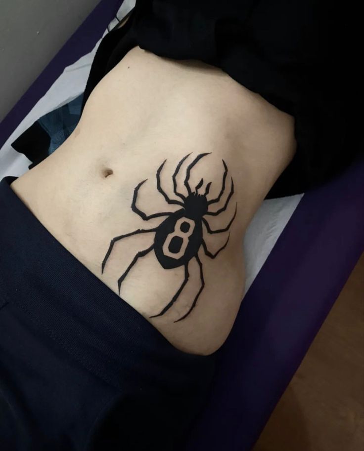 a woman's stomach with a black spider tattoo on her side and the letter b