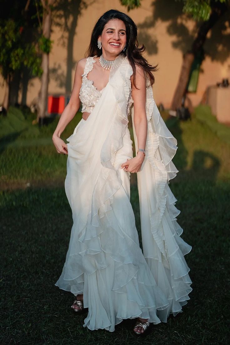 📌Hey! Please message us if you have any questions. We'll definitely assist you. This gorgeous white organza ruffle saree will elevate your sense of fashion and comes with a full-sequence blouse. The feminine touch that the tiny ruffles and translucent organza fabric bring to the entire design. The saree is skilfully made to drape nicely and provide a style that exudes easy charm. The full-sequence blouse gives this already gorgeous ensemble the perfect amount of glitz and shine. Onlookers will be amazed by the detailed sequence work, which is likely to catch the light. The blouse is made to fit precisely and improve the saree's overall appearance. This saree is a genuine showstopper and is ideal for weddings, parties, or any special occasion. With this classy and refined combination, you' Saree Modern Party Wear, Anjali Saree, Organza Ruffle Saree, Ruffle Saree Designs, Pelli Sarees, Farewell Saree, Lehanga Saree, Ruffled Saree, Function Dress