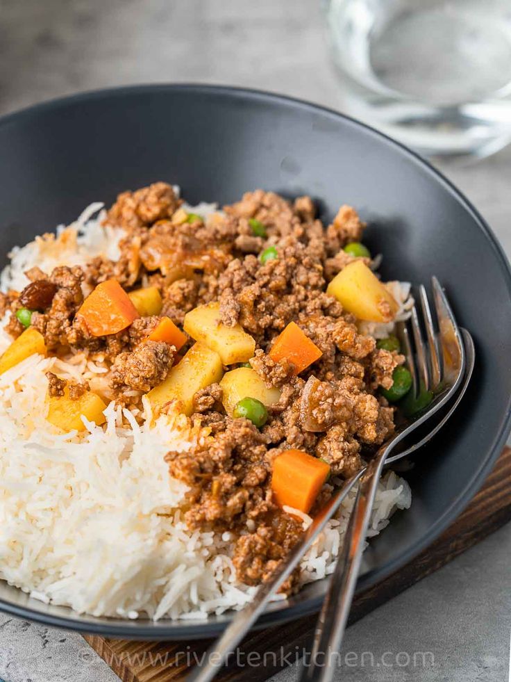 a black plate topped with rice and ground beef next to a glass of water on a wooden table