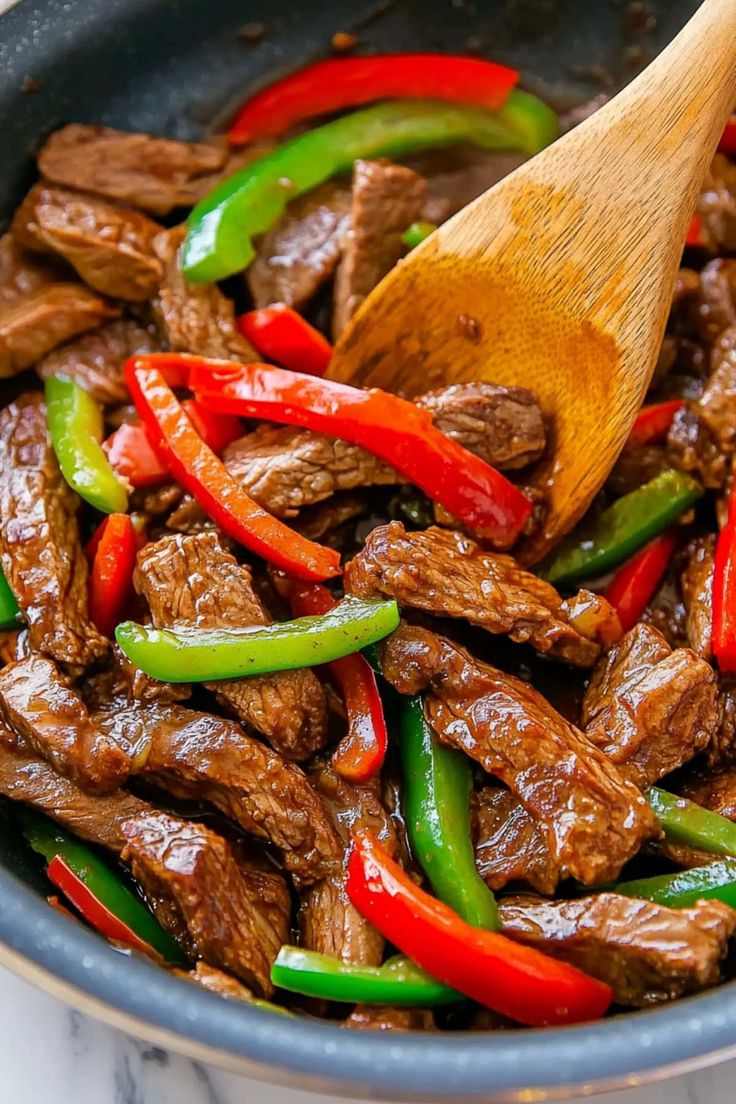 beef and peppers in a skillet with a wooden spoon