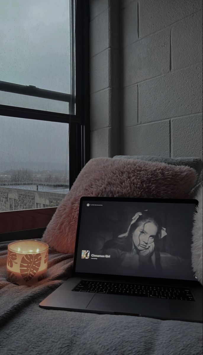 an open laptop computer sitting on top of a bed next to a candle and window