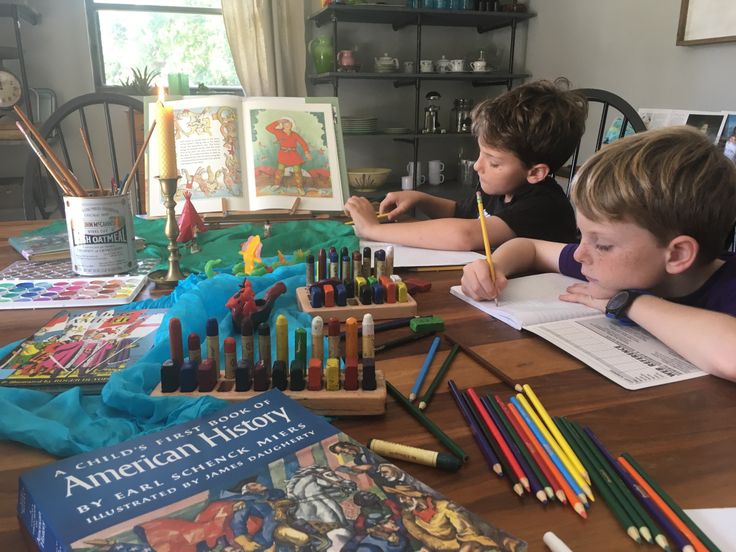 two boys sitting at a table with books and crayons in front of them