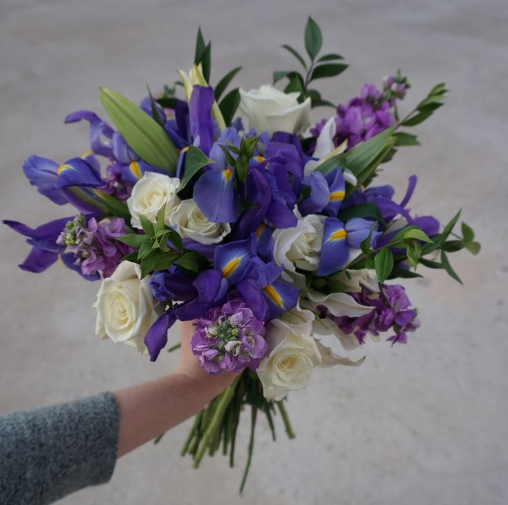 a bouquet of purple and white flowers in someone's hand