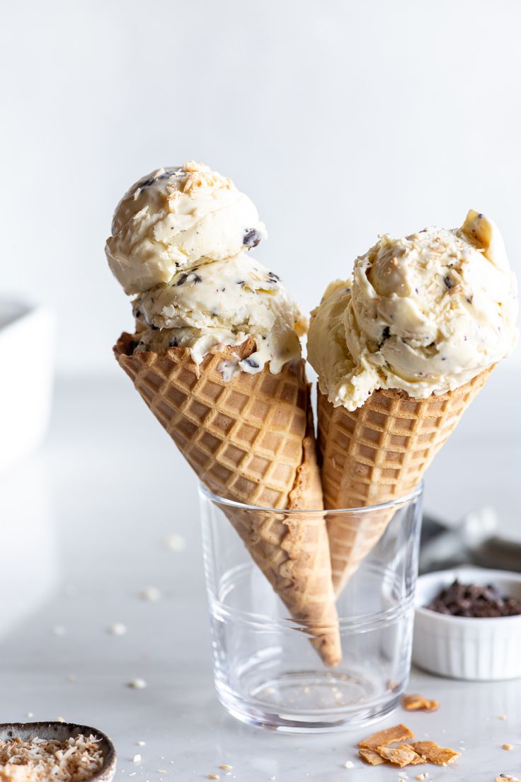 two scoops of ice cream sit in a glass on a white surface with other ingredients