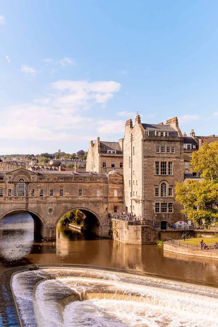 an old stone bridge over a river with water flowing under it and buildings in the background