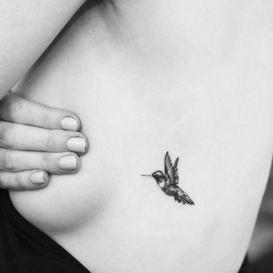 a black and white photo of a woman's stomach with a small hummingbird tattoo on it