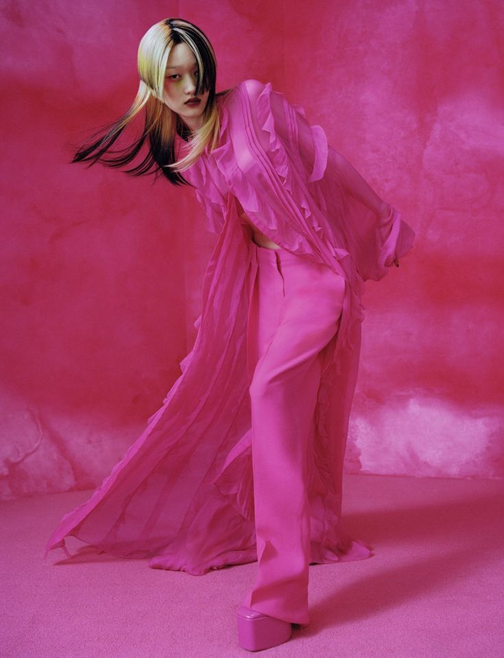 a woman in a pink dress with long hair standing on a pink floor and looking off to the side