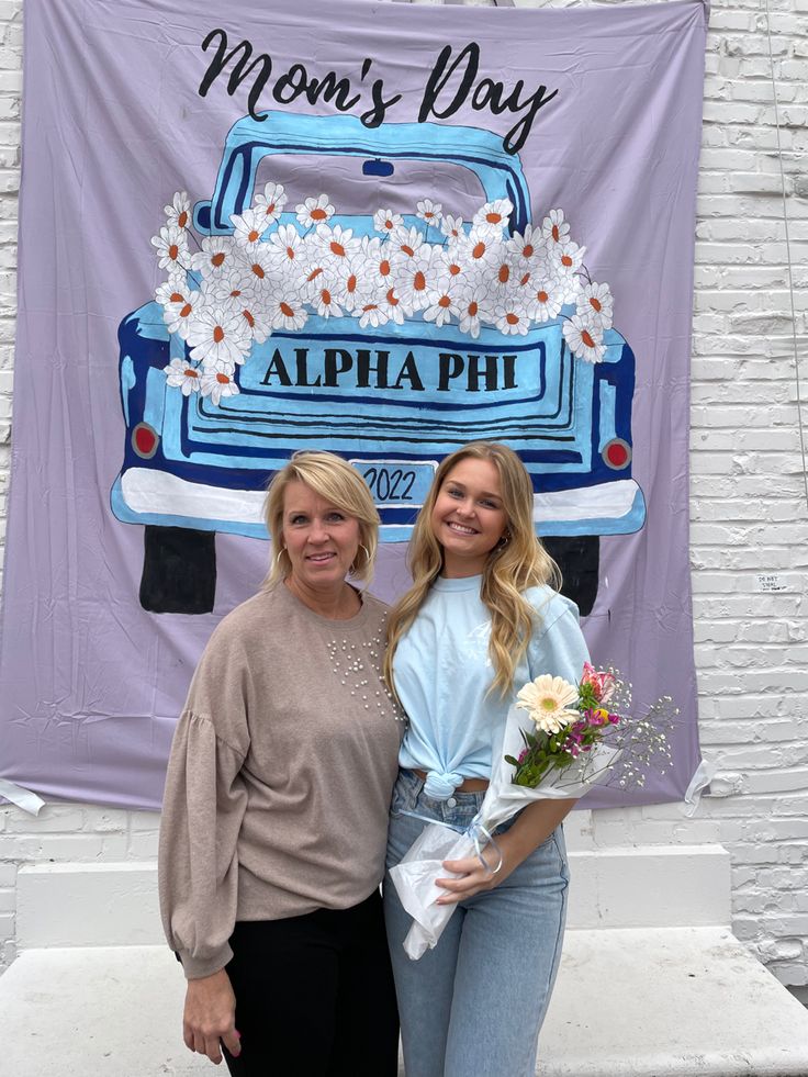 two women standing next to each other in front of a sign that says mom's day