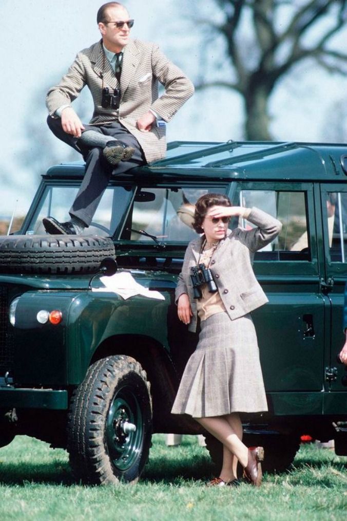 two people standing in front of an old green land rover with the driver sitting on it's roof