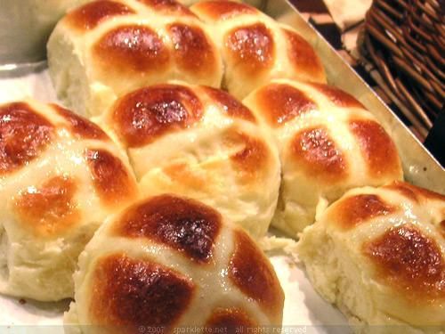 hot cross buns sitting in a basket next to some breadsticks on a table