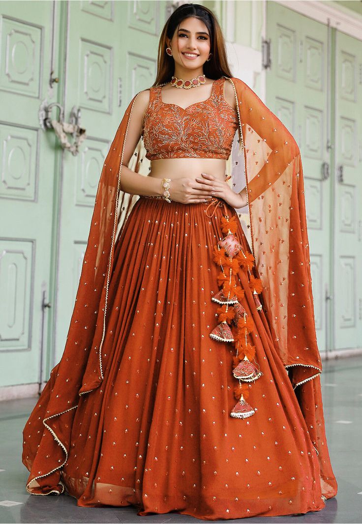 Faux Georgette Lehenga in Orange This attire with Cotton and Shantoon Lining is Enhanced with Fancy Tassels, Resham, Thread, Zari and Sequins Work Available with a Unstitched Faux Georgette Orange Choli and a Faux Georgette Dupatta in Orange The Semi-Stitched Lehenga Waist and Hips are Customizable from 24 to 62 inches and from 28 to 66 inches respectively and Lehenga Length is 38 to 42 inches Do Note: Accessories shown in the image are for presentation purposes only. (Slight variation in actual Georgette Embroidery Lehenga, Orange Lehenga Choli, Crop Blouse Designs For Lehenga, Terracotta Lehenga, Orange Chaniya Choli For Navratri, Lehenga Models For Stitching, Orange Traditional Outfits, Mehendi Look For Bridesmaid, Rust Colour Lehenga