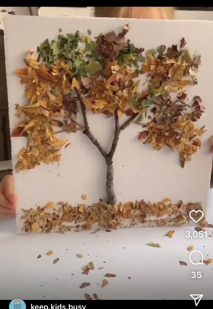 a child holding up a piece of paper that has a tree made out of leaves on it