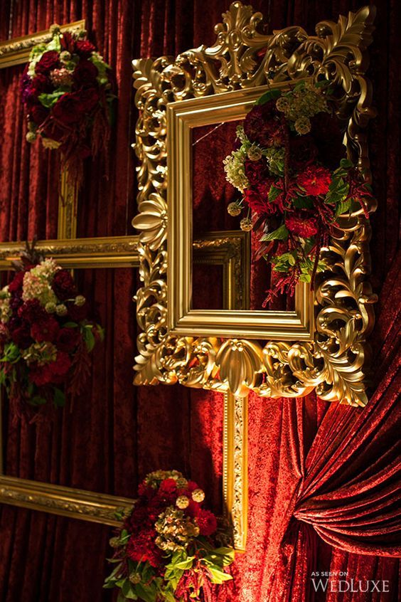 red and gold wedding decor with flowers on the wall in front of it, along with an ornate framed mirror