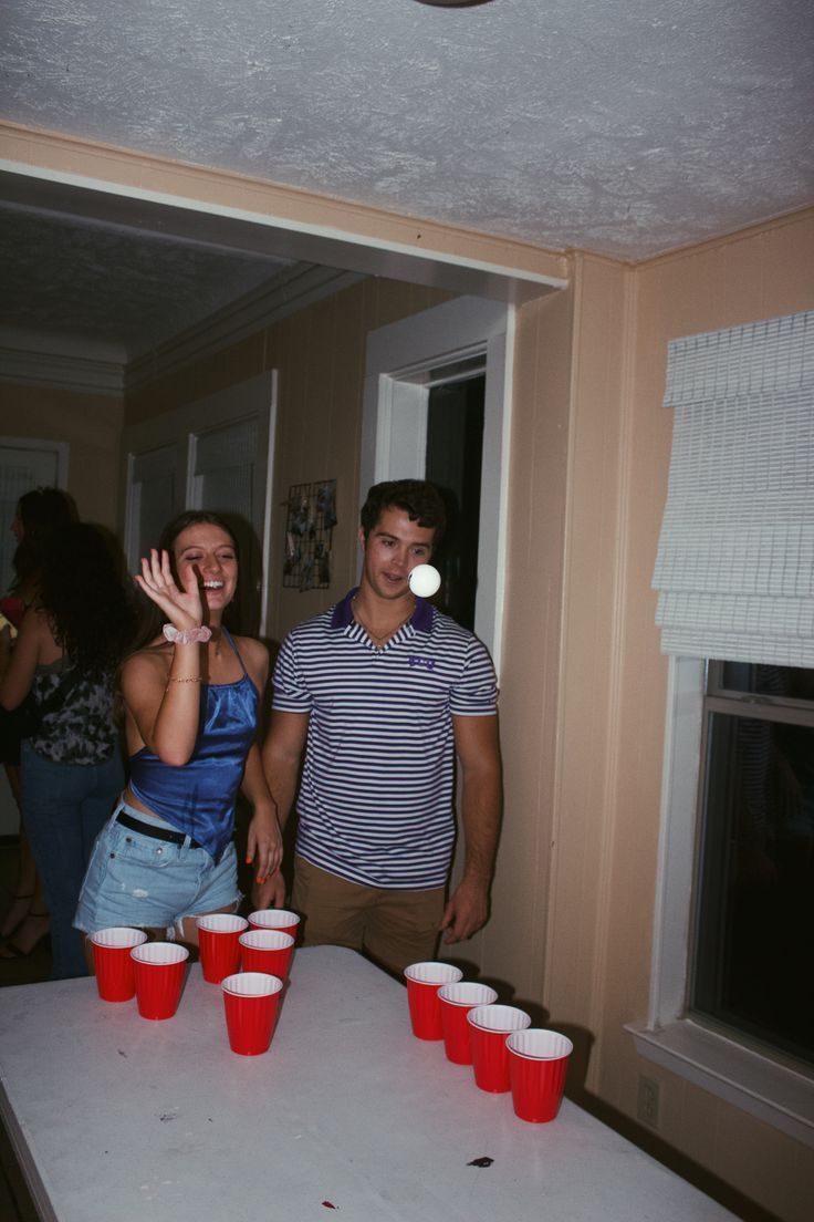 two people standing in front of a table with red cups on it and one person throwing a frisbee