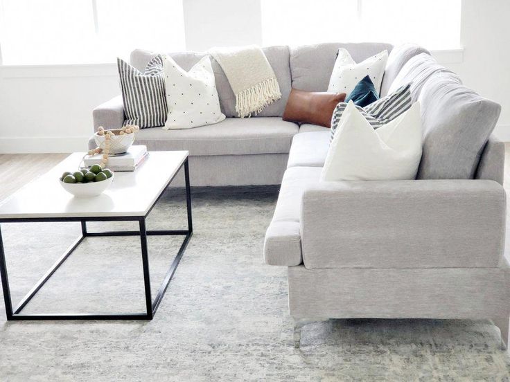 a living room with couches, tables and pillows on the floor in front of windows