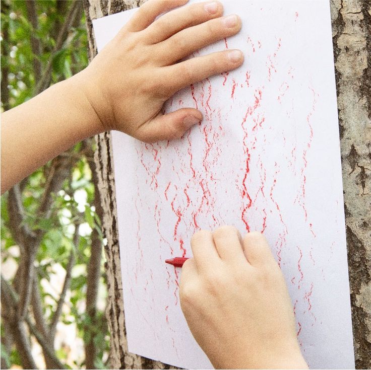 two hands are drawing on a piece of paper with red crayons in front of them