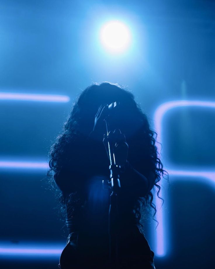 a woman with curly hair holding a microphone in front of a stage light and lights behind her