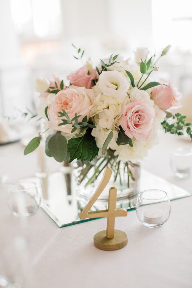 a centerpiece with flowers and greenery is displayed on a table in front of wine glasses