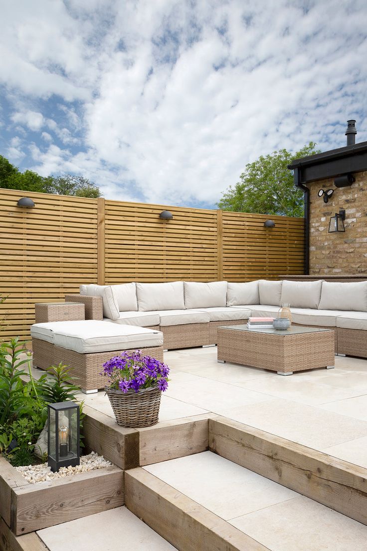 an outdoor seating area with flowers and plants in the foreground, next to a wooden fence