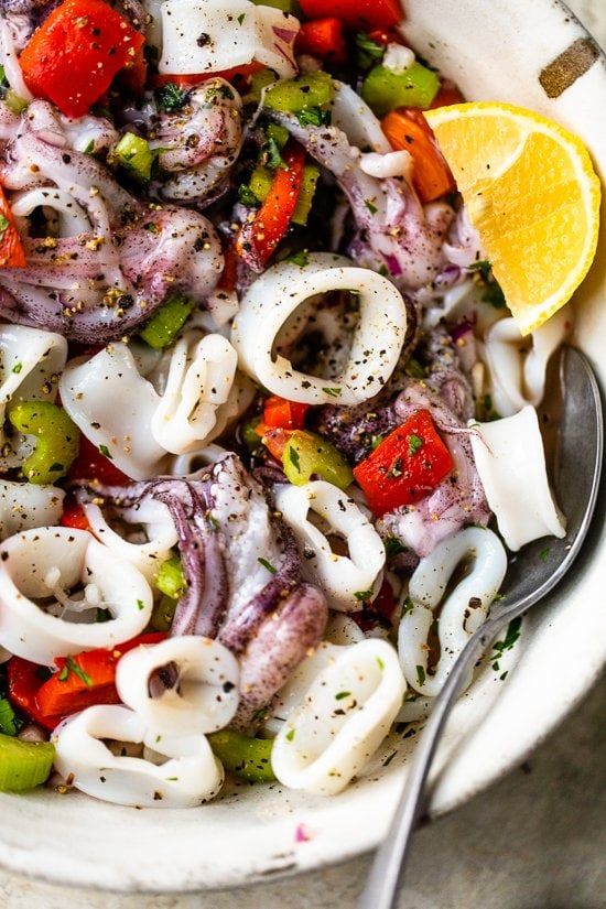 an octopus pasta salad in a bowl with a fork and lemon wedge on the side