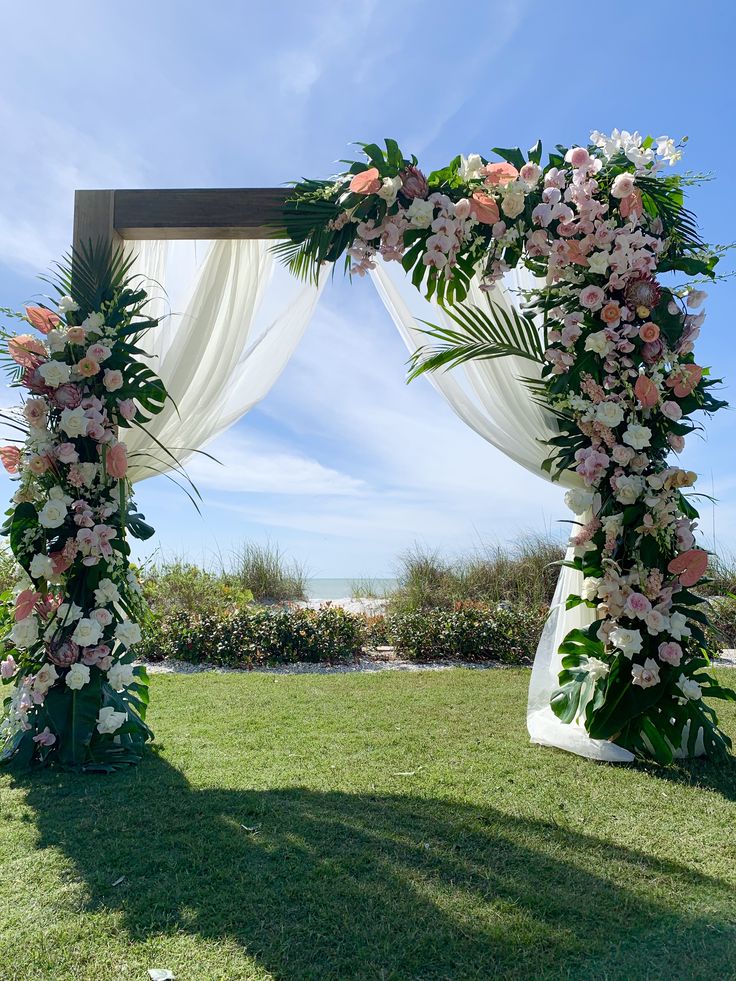 a wedding arch decorated with flowers and greenery on the lawn at a beach resort