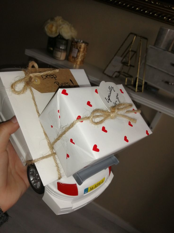 a hand holding a white gift box with hearts on it and string tied around the top