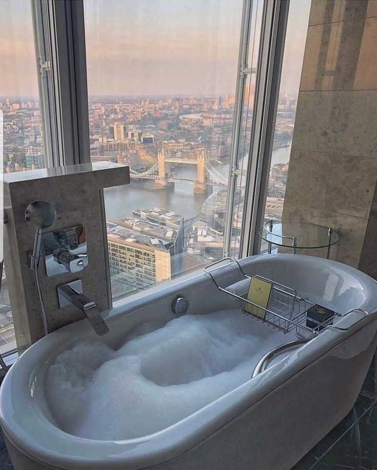 a bathtub with foam on the floor in front of a window overlooking a city