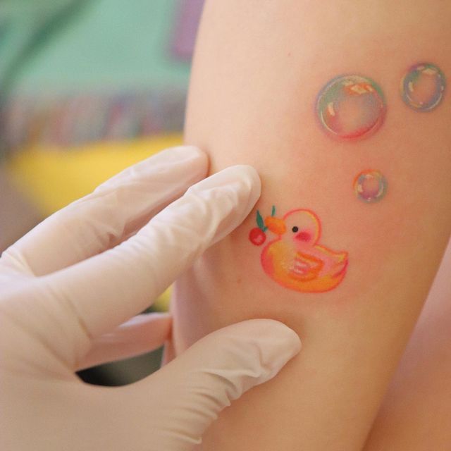 a person holding up a small tattoo with water droplets on it and an orange rubber duck